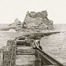 The north end of the beach railway as it swings around the cliff, built in 1899 to transport sand and gravel to the blockyards at the dock where the huge concrete blocks were made for the building of the piers. After several deaths, the last in July 1933 when Wm Fisher aged 9 fell into the water and drowned, it was demolished in the 1933. Photograph c1930.