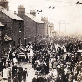 There were no First World War victory celebrations when the fighting stopped in November 1918 because it was only an armistice. The official 'Peace Processions' were held in July 1919 and this photograph is of the East End procession in Prospect Row. The photographer is standing at an upstairs window of the 'Welcome Tavern' at the south end of Barrack Street and looking down the Prospect Row towards the Quadrant. The Corporation tramlines and overhead wires lead off to the right towards the Docks terminus. This tram route did not make a profit and was abandoned in 1928.