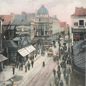 MACKIE'S CORNER:
An unused and, therefore, undated postcard but obviously the early 1900s.
A photograph taken from Blackett's corner. The building on the immediate right is the entrance to the north end of the Railway Station. The name Mackie's Corner derives from a silk hat manufacturer of the early 19th century. The address was actually Nos 1 & 2 Hutchinsons Buildings and was known as a 'Hatting Establishment'. There are several horsedrawn carts in evidence and notice the single deck tramcar crossing from Fawcett Street to Bridge Street.
Todds apparently sold blankets, gloves and furs. Opposite Todds is Walkers the opticians and jewellers. Adjacent to them is J.Coopers and Sons boot and shoe shop. Their trademark was a beehive and it can be seen on the corner of the third storey of the building level with and to the right of the word 'SONS'.