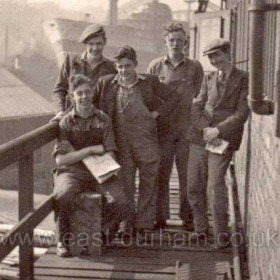 Joiners Shop, J L Thompson's Shipyard
Sitting, Alf Redford,   Standing from the left, Alec Mackie,  not known,  
Dickie Knowles,  Terry Hogan.   

J L THOMPSONS SHIPYARD was where the Glass Centre is now,  It had 3 or 4 berths where the ships were built, then they went to Manor Quay for fitting out. The photo shows us sitting on the 2nd floor balcony of the joiners shop at the Manor Quay with a ship in the back ground at Dickensons Quay where the big crane had lifted in the ships engine,  you can see Wearmouth Bridge in the background.     (1945 / 46)
Photograph and caption from Alf Redford