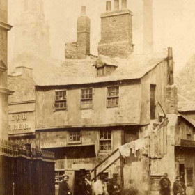 The sign on the corner of the building above the two men at centre reads Cow Gate to the left.