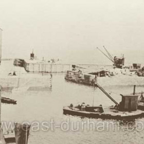 Photograph of the new dredger in the South Dock 1876. George Hardy wrote "We did much to facilitate the removal of sand from the harbour entrance. We fitted up a keel-craft to float to the position required, either inside or at outside of the dock, where it could clear away ship's berths in any corner of the dock. This craft was fitted with crane and dredging lifting grab. We also erected a portable crane on the end of the south pier, with suitable railway and change wheels, in order to reach any part of the channel and thus remove sand even when the sea was rough."