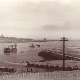 This postcard of the harbour at South Shields dates from about 1905. The trucks in the foreground are full of stone from the Trow Rocks quarry, near the present Gypsy's Green Stadium at the south end of the promenade. The stone is being shipped across the river to repair the breached north pier, where the crane can be seen working in the background. The 'Marsden Rattler' pub (now renamed) was built on the line of the quarry railway but the real 'Rattler' line was further south. Caption from Malcolm Fraser.