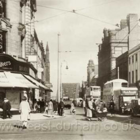 Bridge Street, looking north towards the Wearmouth Bridge in 1939. Judging from the shadows its about ten in the morning and the street is already busy. An Austin saloon car, registered in London in 1935, heads a line of traffic waiting for the lights to change at Mackies corner. The Corporation double-deck bus is a Daimler and probably about a couple of years old. The tram behind it came was bought from Huddersfield in 1938 had been one of their most luxurious trams. It has just passed the Grand Hotel, one of the town’s most prestigious venues at that time.    Info from Malcolm Fraser